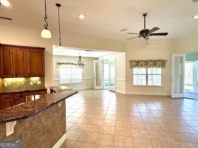 kitchen featuring hanging light fixtures, dark stone counters, a kitchen bar, light tile patterned flooring, and ceiling fan with notable chandelier