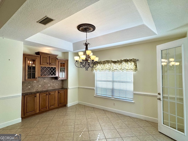 kitchen with tasteful backsplash, a raised ceiling, light tile patterned floors, a chandelier, and hanging light fixtures