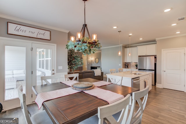 dining area featuring sink, an inviting chandelier, light wood-type flooring, and ornamental molding