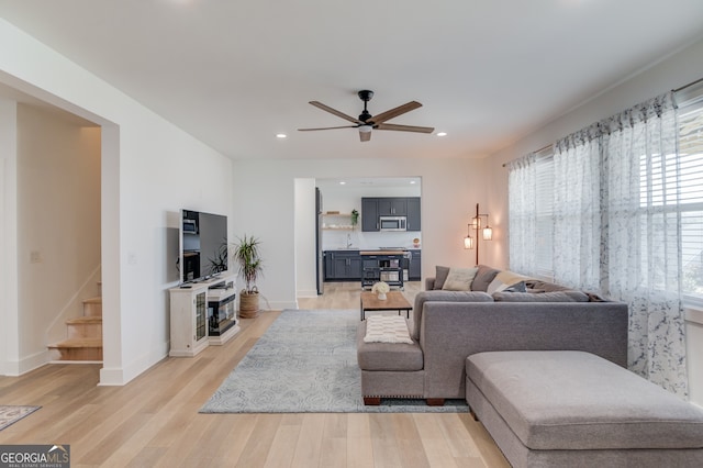 living room featuring ceiling fan, sink, and light wood-type flooring