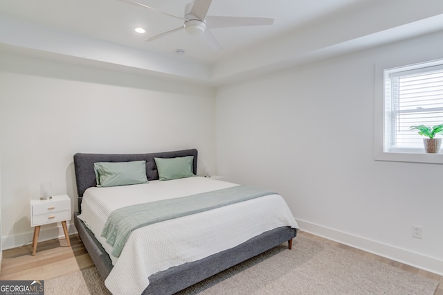 bedroom with ceiling fan, light hardwood / wood-style floors, and a tray ceiling