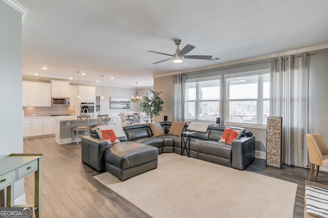 living room featuring crown molding, ceiling fan with notable chandelier, and light wood-type flooring