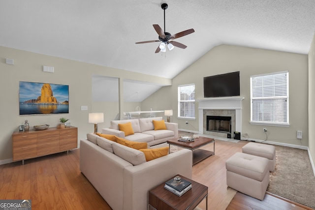 living room with ceiling fan, light hardwood / wood-style flooring, vaulted ceiling, and a fireplace