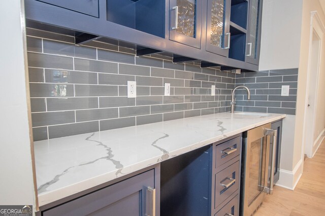 kitchen featuring backsplash, sink, light stone countertops, light hardwood / wood-style floors, and beverage cooler