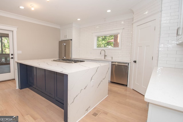 kitchen featuring white cabinetry, sink, light stone counters, a kitchen island, and appliances with stainless steel finishes