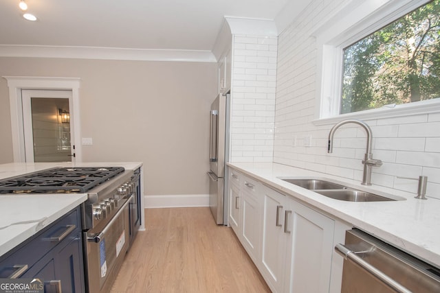 kitchen with decorative backsplash, light stone counters, sink, high quality appliances, and white cabinetry