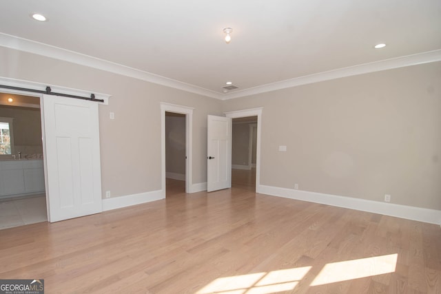 interior space with ensuite bathroom, a barn door, ornamental molding, and light hardwood / wood-style flooring