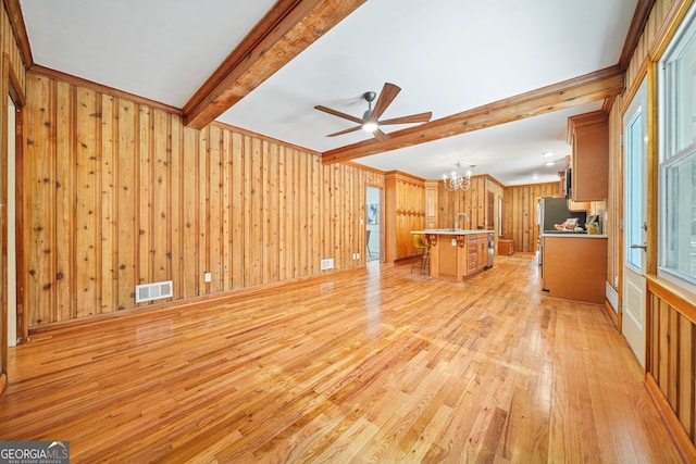 unfurnished living room with sink, beamed ceiling, wood walls, ceiling fan with notable chandelier, and light wood-type flooring