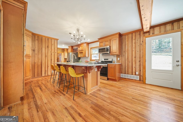 kitchen featuring light hardwood / wood-style floors, a kitchen island with sink, appliances with stainless steel finishes, and a chandelier