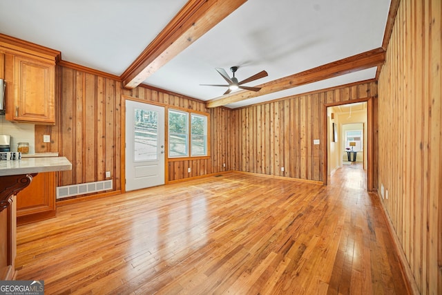 unfurnished living room with beamed ceiling, light wood-type flooring, ceiling fan, and wood walls