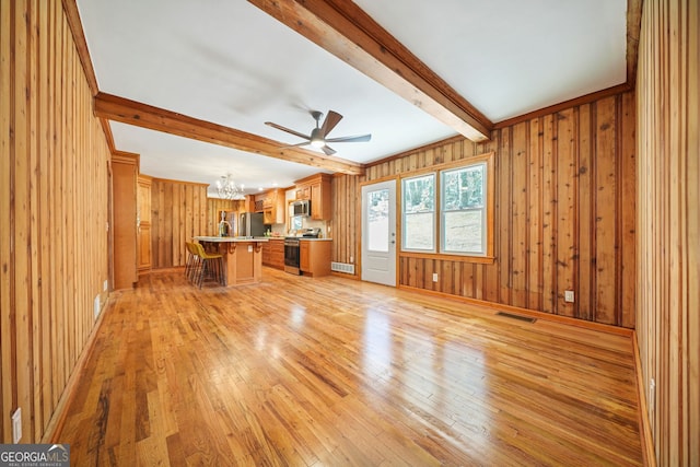 unfurnished living room featuring beam ceiling, wooden walls, light hardwood / wood-style flooring, and ceiling fan with notable chandelier