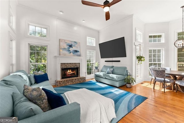 living room with ornamental molding, ceiling fan with notable chandelier, wood-type flooring, a fireplace, and a high ceiling