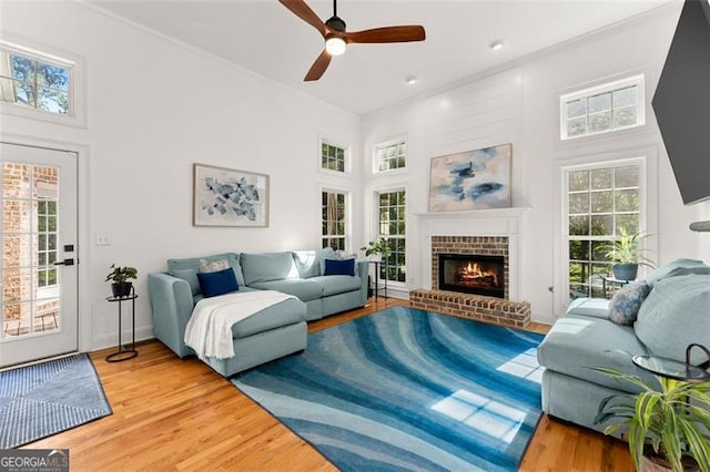 living area featuring light wood-style flooring, a brick fireplace, a ceiling fan, and plenty of natural light