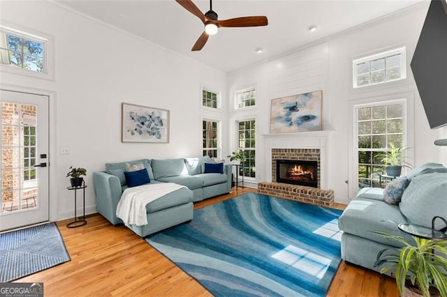 living room featuring hardwood / wood-style floors, a towering ceiling, a brick fireplace, and ceiling fan