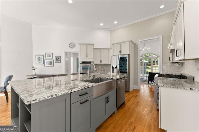 kitchen with gray cabinetry, stainless steel appliances, decorative backsplash, light stone counters, and a kitchen island with sink