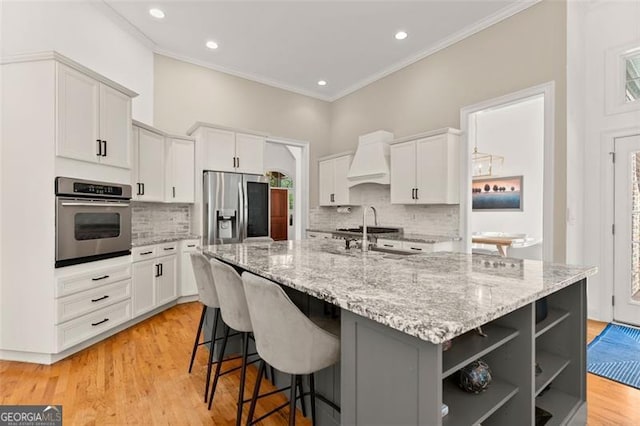 kitchen featuring white cabinets, stainless steel appliances, custom exhaust hood, and an island with sink