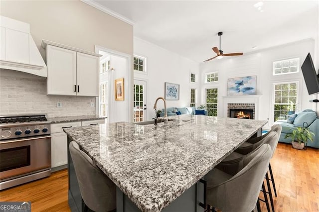 kitchen with custom exhaust hood, a breakfast bar, high end range, white cabinets, and tasteful backsplash