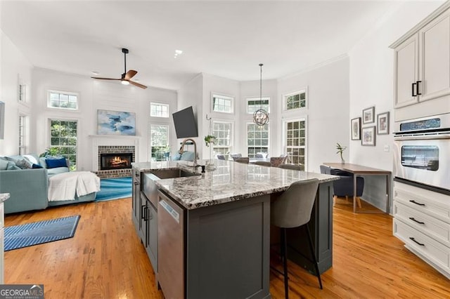 kitchen featuring appliances with stainless steel finishes, sink, a center island with sink, decorative light fixtures, and a fireplace