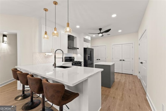 kitchen with kitchen peninsula, a kitchen breakfast bar, wall chimney exhaust hood, black appliances, and hanging light fixtures