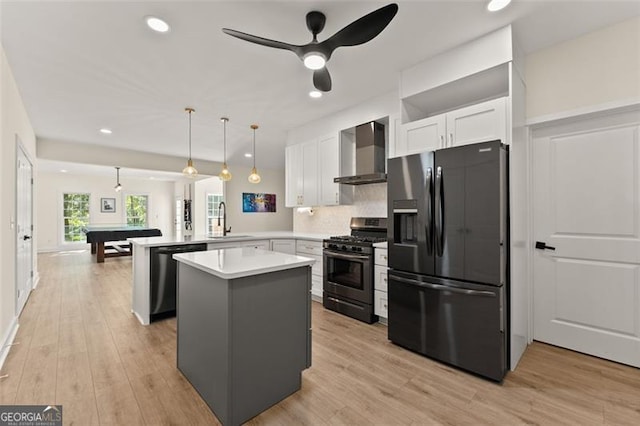 kitchen featuring kitchen peninsula, appliances with stainless steel finishes, wall chimney range hood, decorative light fixtures, and white cabinets