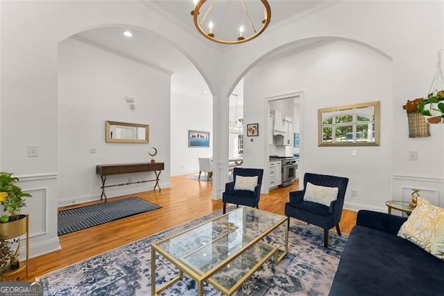living area with arched walkways, a notable chandelier, ornamental molding, and wood finished floors