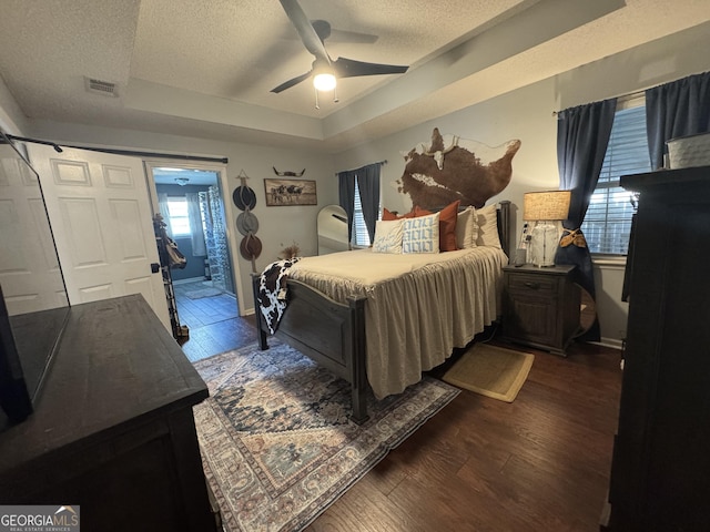 bedroom featuring ceiling fan, dark hardwood / wood-style flooring, a raised ceiling, and a textured ceiling