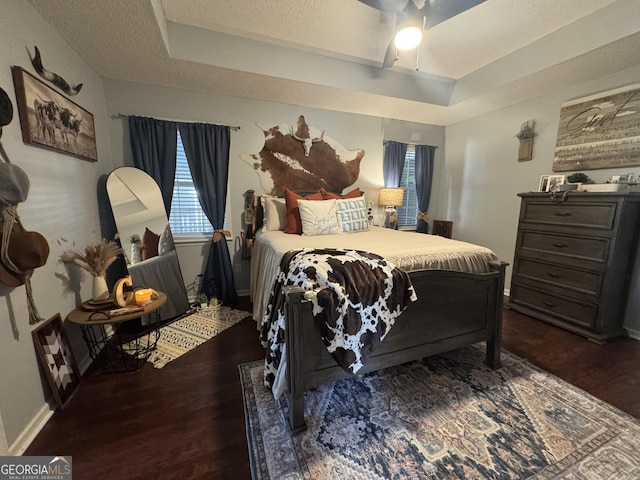 bedroom featuring a textured ceiling, ceiling fan, a tray ceiling, and dark wood-type flooring