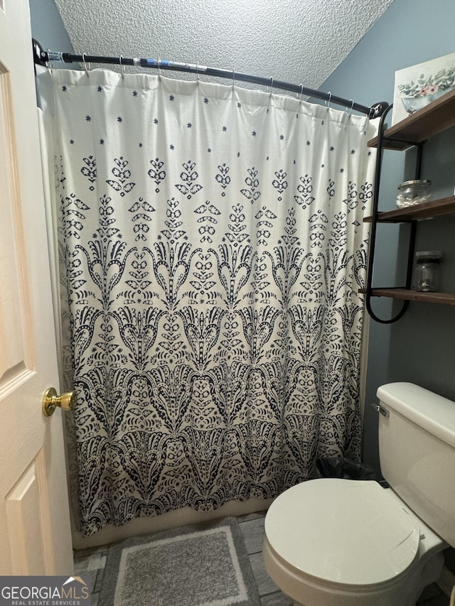 bathroom featuring toilet, a shower with shower curtain, and a textured ceiling