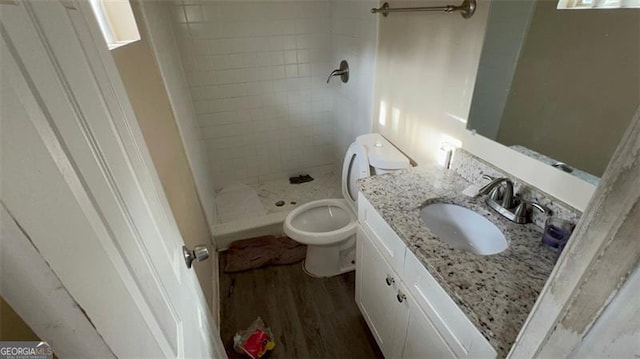 bathroom with a tile shower, vanity, hardwood / wood-style flooring, and toilet