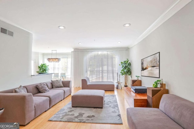 living room with light wood-type flooring, crown molding, and a notable chandelier