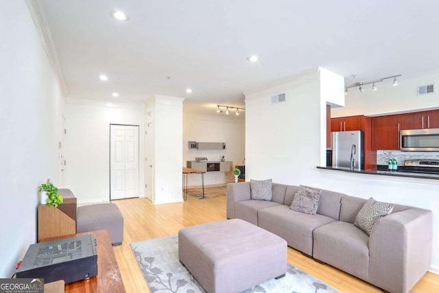 living room with light wood-type flooring, track lighting, and ornamental molding