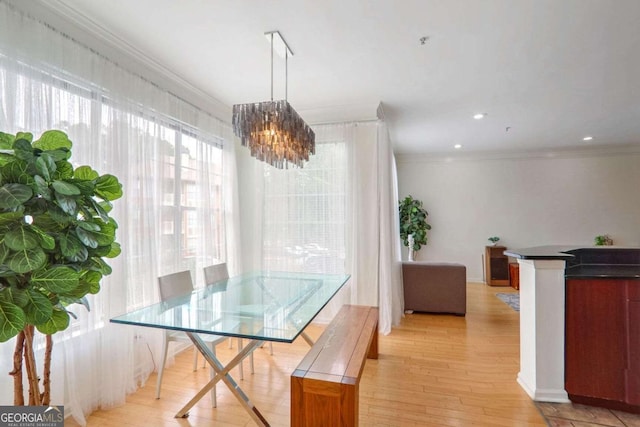 dining space featuring light wood-type flooring, ornamental molding, and a notable chandelier