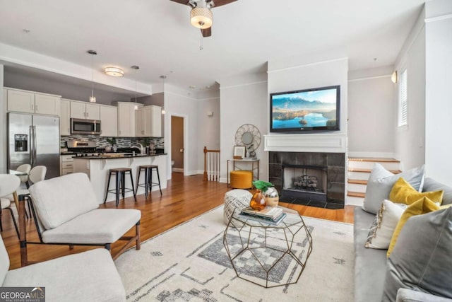 living room with a tile fireplace, ceiling fan, sink, and light hardwood / wood-style floors