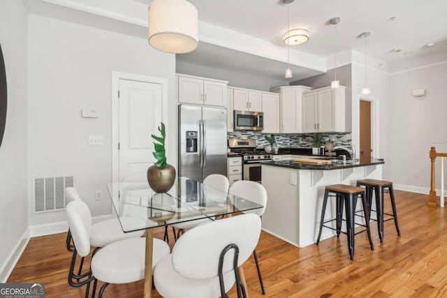 kitchen with white cabinetry, stainless steel appliances, a kitchen breakfast bar, decorative light fixtures, and decorative backsplash