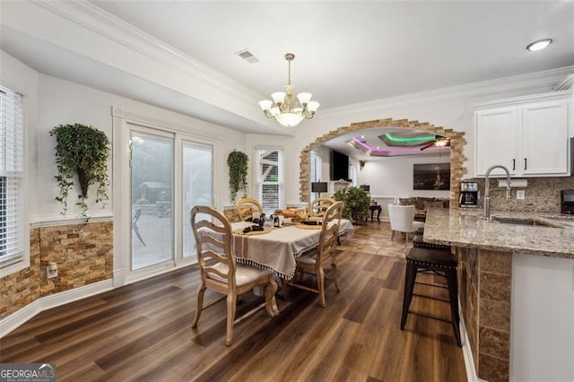 dining area with sink, dark hardwood / wood-style flooring, crown molding, a tray ceiling, and ceiling fan with notable chandelier