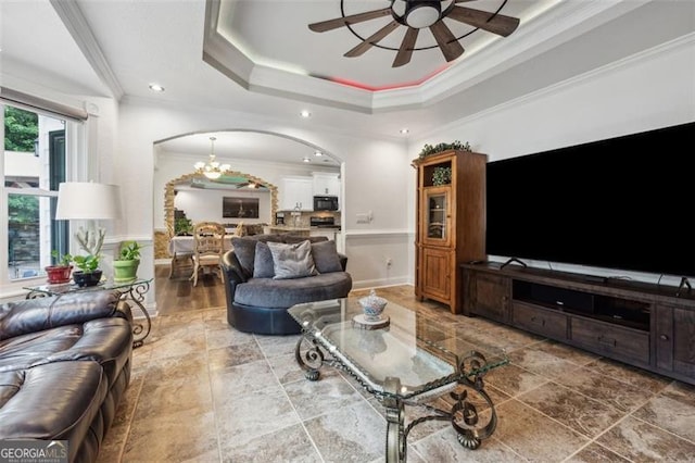 living room featuring ceiling fan with notable chandelier, ornamental molding, and a tray ceiling