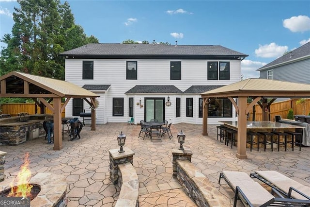 rear view of property with a gazebo, a bar, an outdoor fire pit, and a patio area