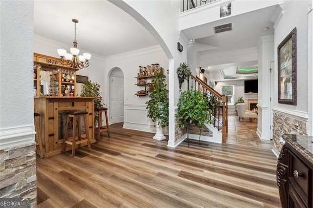 entrance foyer with hardwood / wood-style flooring, ornamental molding, bar area, and a chandelier