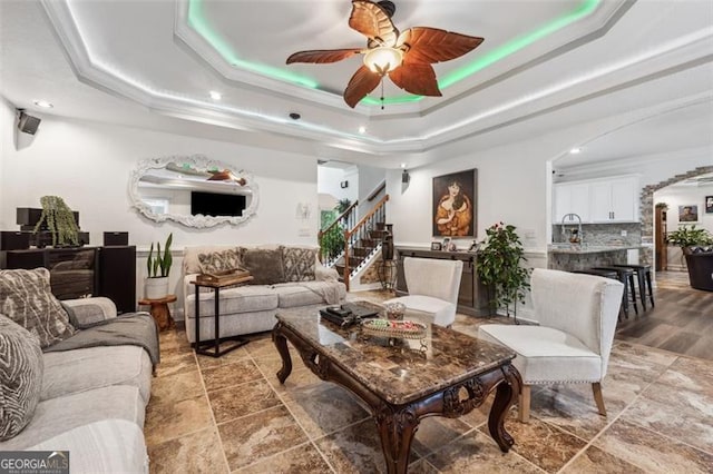 living room with a raised ceiling, ceiling fan, sink, and ornamental molding