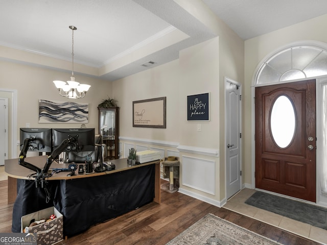 foyer entrance featuring a raised ceiling, ornamental molding, wood-type flooring, and an inviting chandelier