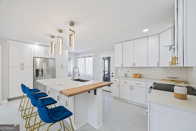 kitchen featuring white cabinetry, stainless steel fridge, a kitchen island with sink, and sink