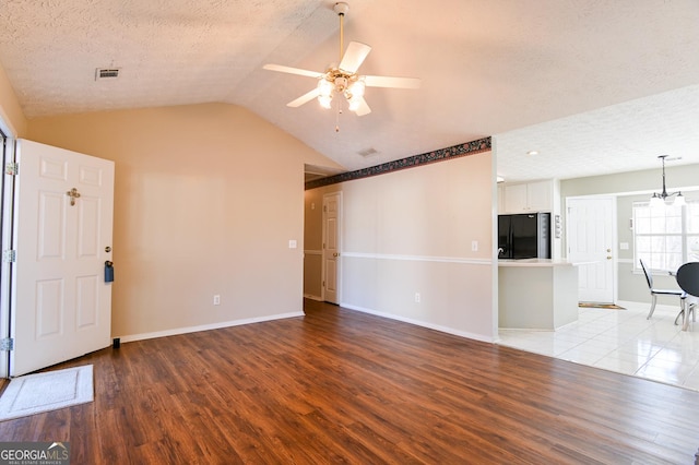 unfurnished living room featuring a textured ceiling, ceiling fan with notable chandelier, light hardwood / wood-style floors, and vaulted ceiling