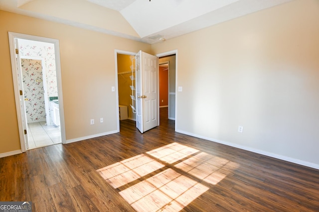 unfurnished bedroom with vaulted ceiling, ensuite bathroom, a spacious closet, and dark wood-type flooring