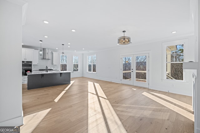 unfurnished living room with crown molding, sink, light hardwood / wood-style floors, and french doors