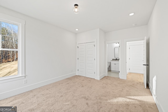 unfurnished bedroom featuring light carpet, ensuite bathroom, and a closet