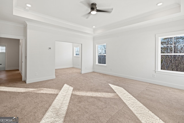 carpeted empty room featuring a tray ceiling, crown molding, ceiling fan, and a healthy amount of sunlight