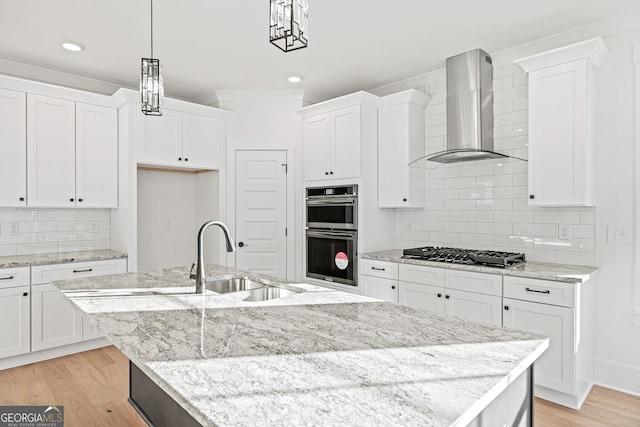 kitchen with wall chimney range hood, an island with sink, pendant lighting, white cabinets, and appliances with stainless steel finishes