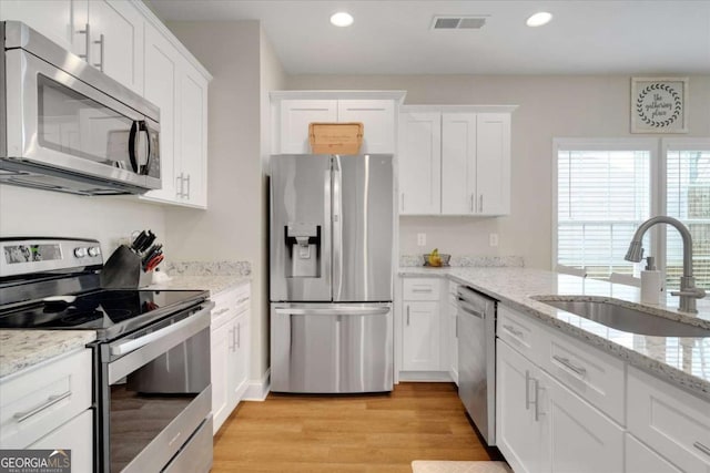 kitchen with appliances with stainless steel finishes, light hardwood / wood-style flooring, white cabinetry, and sink