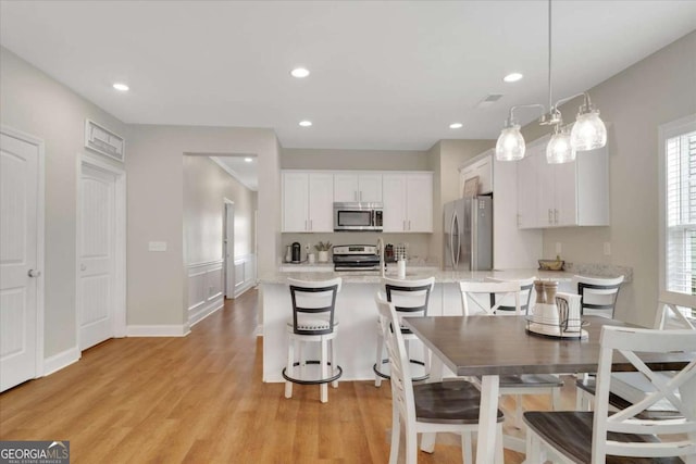 kitchen with white cabinets, hanging light fixtures, light hardwood / wood-style flooring, light stone counters, and stainless steel appliances