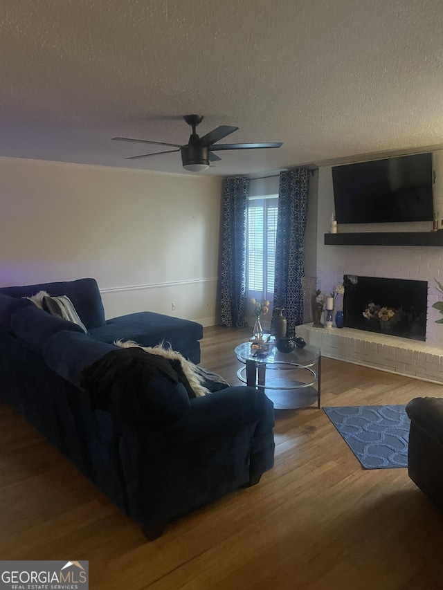 living room featuring hardwood / wood-style floors, a fireplace, ceiling fan, and a textured ceiling